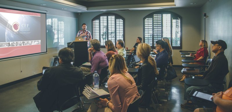 A group of smartly-dressed professionals watching a PowerPoint presentation in a well-lit room.